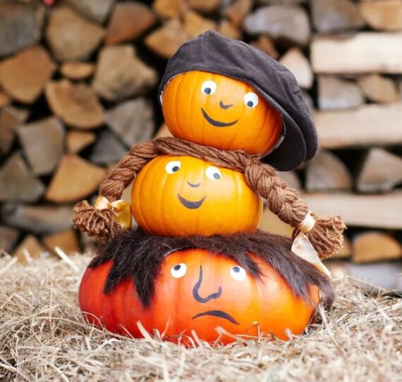 Stacked pumpkins decorated with painted faces, hats and hair for a playful look.