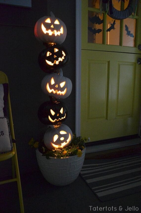 Pumpkins piled high with glowing lantern faces next to a door.