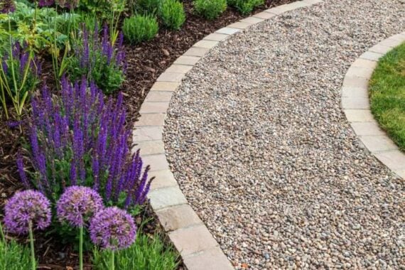 Curving gravel garden path surrounded by stone borders and purple flowering plants