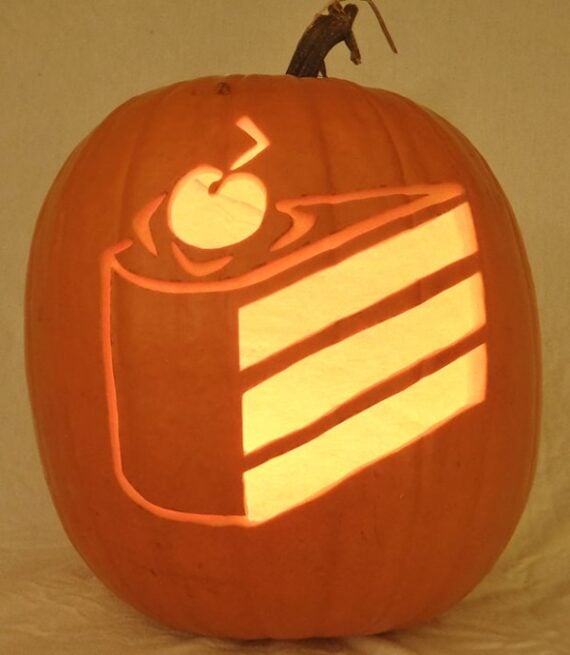 Pumpkin carved with a glowing slice of cake topped with a cherry.