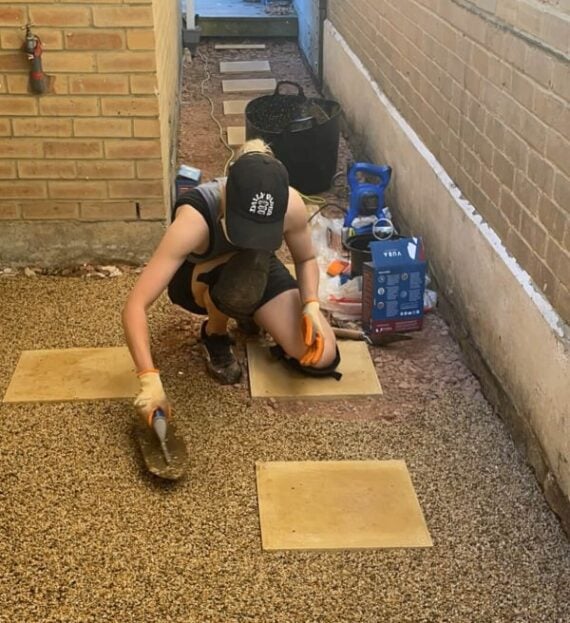 Man installing square pavers in a pea gravel side yard