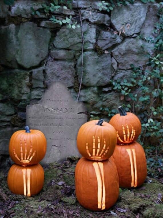Pumpkins carved with glowing skeleton hands and thorns in an eerie graveyard scene.
