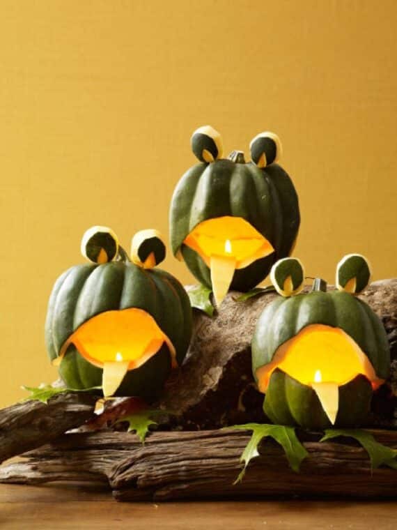 Green pumpkins carved into frog faces with candles glowing inside.