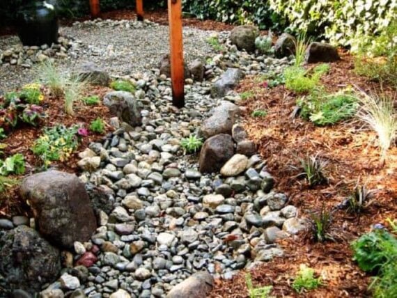 DIY rock lined french drain that runs through a landscaped garden bed