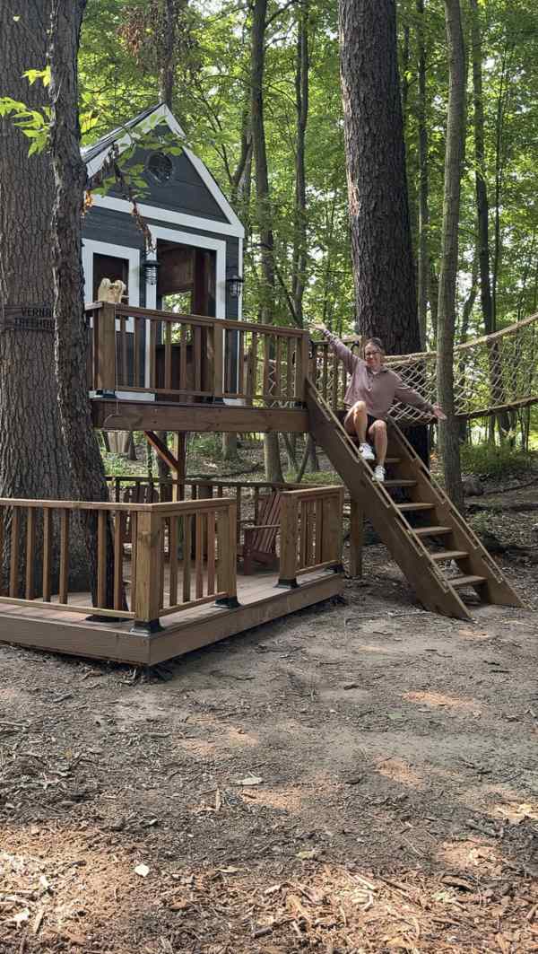DIY backyard tree house with deck platform, stairs and hammock bridge built between trees.
