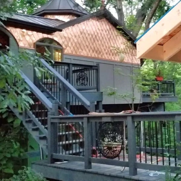 Decorative treehouse with copper roof and deck built among lush forest trees.