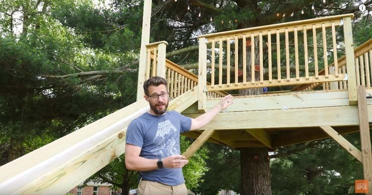 DIY backyard treehouse platform with stairs and wooden railing built around a large tree.