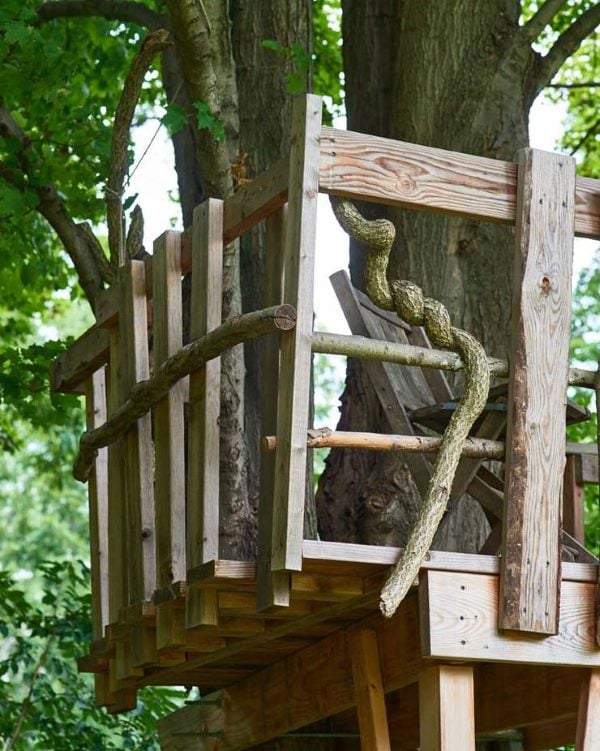 Simple DIY treehouse platform with wooden railing and natural branch ladder.